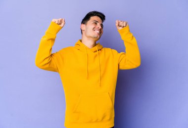 Mor arka planda izole genç beyaz adam özel bir günü kutluyor, atlıyor ve enerjiyle kollarını kaldırıyor..