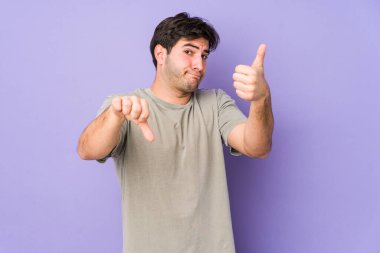 Mor arka planda izole edilmiş genç adam, baş parmağını kaldırıyor, zor bir seçim konsepti.