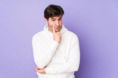 Mor arka planda izole edilmiş genç adam şüpheli ve şüpheci bir ifadeyle yana bakıyor..