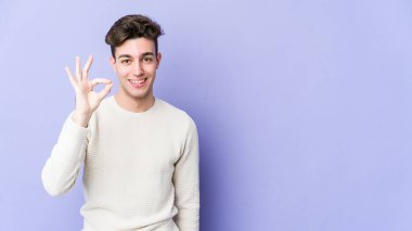 Genç beyaz adam mor arka planda izole edilmiş neşeli ve kendinden emin, iyi bir jest yapıyor..