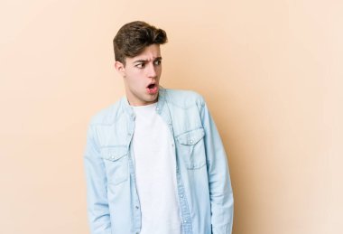 Beyazlı genç bir adam bej arka planda izole edilmiş. Gördüğü bir şey yüzünden şok oluyor..