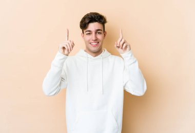 Beyazlı genç bir adam bej arka planda izole edilmiş iki parmağı da boş bir alan gösteriyor..