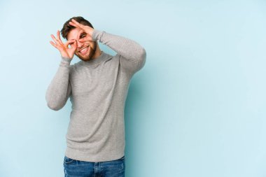 Mavi arka planda izole edilmiş genç beyaz adam gözlerinde sorun olmadığını gösteriyor.