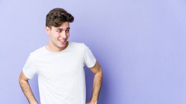 Mor arka planda izole edilmiş genç beyaz adam gülüyor ve gözlerini kapıyor, rahatlamış ve mutlu hissediyor..