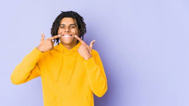 Genç Afrikalı Amerikalı Rasta adam gülümsüyor, parmaklarını ağıza doğrultuyor..