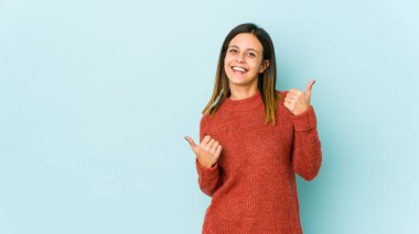 Mavi arka planda izole edilmiş genç bir kadın iki parmağını da kaldırıyor, gülümsüyor ve kendinden emin..