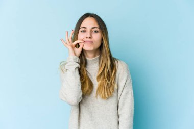 Mavi arka planda izole edilmiş genç beyaz kadın parmakları dudaklarında bir sır saklıyor..