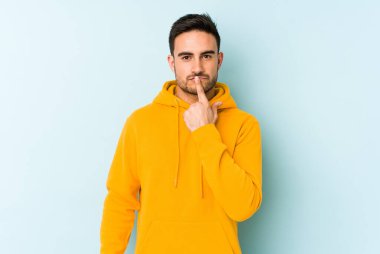 Kafkasyalı genç adam mavi arka planda izole edilmiş düşünüyor ve bakıyor, yansıtıyor, düşünüyor, bir fantezi kuruyor..