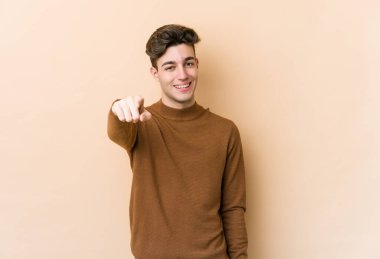 Beyaz tenli genç adam bej arka planda izole edilmiş. Önü işaret eden neşeli gülümsemeler..