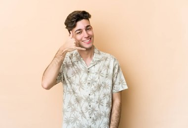 Beyazlı genç bir adam bej arka planda izole edilmiş. Cep telefonu hareketini parmaklarıyla gösteriyor..