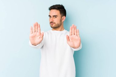 Mavi arka planda izole edilmiş genç beyaz adam elini uzatmış, dur işareti göstererek seni engelliyor..