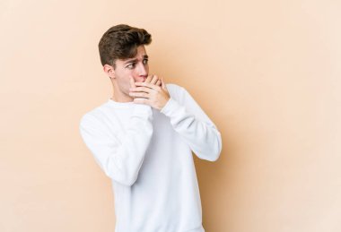 Beyazlı genç bir adam bej arka planda izole edilmiş. Düşünceli bir şekilde bir fotokopi odasına bakıyor. Ağzını eliyle kapatıyor..