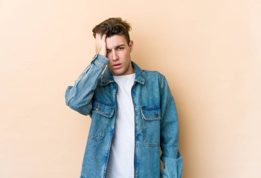 Beyazlı genç bir adam bej arka planda izole edilmiş. Yorgun ve uykulu. Elini başının üstünde tutuyor..