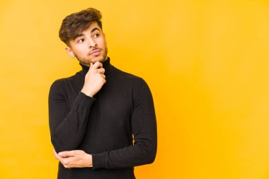 Sarı arka planda izole edilmiş genç bir Arap şüpheli ve şüpheci bir ifadeyle yana bakıyor..