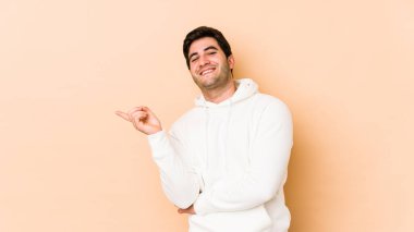 Bej arka planda izole edilmiş genç adam işaret parmağıyla işaret ederek gülümsüyor..