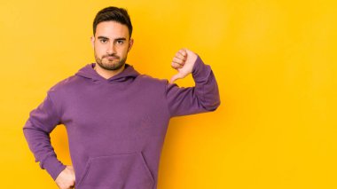 Sarı fırında izole edilmiş genç beyaz adam baş parmağını aşağı gösteriyor, hayal kırıklığı konsepti..