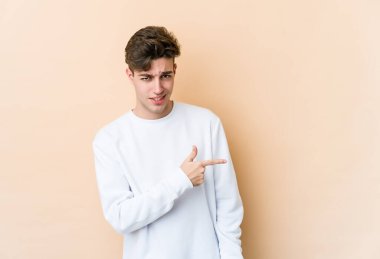 Beyaz tenli genç adam bej arka planda izole edilmiş gülümsüyor ve boş alanda bir şeyler gösteriyor..
