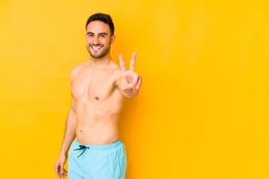 Sarı arka planda mayosu olan genç beyaz bir adam neşeli ve kaygısız genç beyaz bir adam parmaklarıyla barış sembolü gösteriyor..
