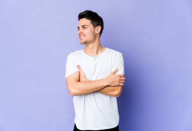 Mor arka planda izole edilmiş genç beyaz adam kollarını kavuşturarak gülümsüyor..