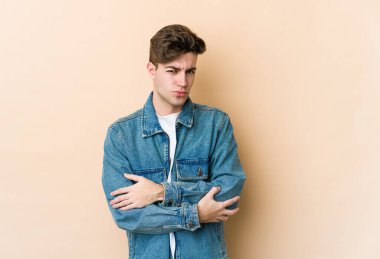 Beyazlı genç adam bej arka planda izole edilmiş. Mutsuz, iğneleyici bir ifadeyle kameraya bakıyor..