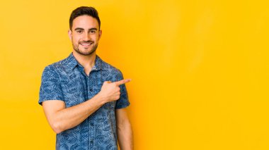 Sarı fırında izole edilmiş genç beyaz adam gülümsüyor ve boş alanda bir şeyler gösteriyor..