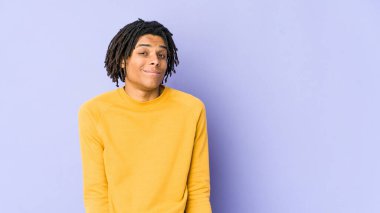 Rasta saç stili giyen genç siyah adam omuz silkiyor ve gözleri açık..