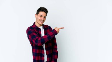 Beyaz arka planda izole edilmiş genç beyaz bir adam gülümsüyor ve boş alanda bir şeyler gösteriyor..