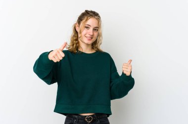 Beyaz arka planda genç beyaz kadın iki parmağını da kaldırıyor, gülümsüyor ve kendinden emin..