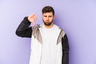 Mor arka planda izole edilmiş genç bir adam, hoş olmayan bir jest gösteriyor, başparmakları aşağıda. Anlaşmazlık konsepti.
