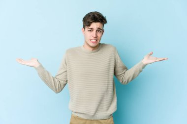 Kafkasyalı genç adam mavi arka planda izole edilmiş. Kafası karışmış ve omuz silkiyor. Kopya alanını tutmak için..
