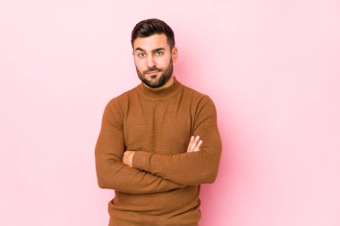 Pembe arka planda genç, beyaz bir adam izole edilmiş. Kameraya alaycı bir ifadeyle bakıyor..