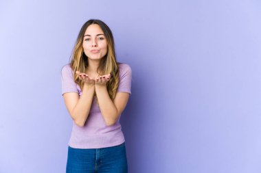 Mor arka planda izole edilmiş beyaz bir kadın dudaklarını katlıyor ve hava öpücüğü vermek için avuç içleri tutuyor..