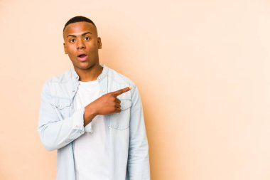 Bej arka planda izole edilmiş genç latin adam yan tarafı işaret ediyor