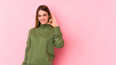 Genç beyaz kadın pembe arka planda izole edilmiş neşeli ve kendinden emin, iyi bir jest yapıyor..