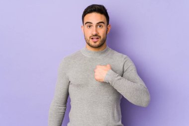 Mor arka planda izole edilmiş genç beyaz adam parmağını göstererek şaşırdı, geniş bir gülümsemeyle..