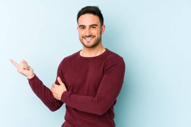 Mavi arka planda izole edilmiş genç beyaz adam işaret parmağıyla işaret ederek gülümsüyor..