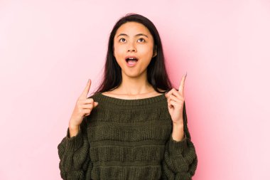 Pembe arka planda izole edilmiş genç Çinli bir kadın ağzı açık bir şekilde üst tarafı işaret ediyor..
