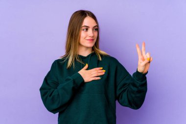 Mor arka planda izole edilmiş genç beyaz kadın yemin ediyor, elini göğsüne koyuyor..