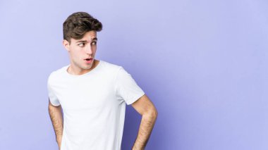 Mor arka planda soyutlanmış genç beyaz adam gülümseyen, neşeli ve keyifli bir tarafa bakıyor..