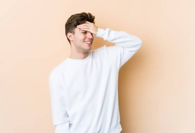 Beyazlı genç bir adam bej arka planda izole edilmiş, mutlu bir şekilde ellerini başının üstünde tutarak gülüyor. Mutluluk kavramı.