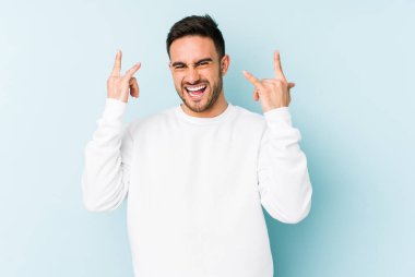 Mavi arka planda izole edilmiş genç beyaz adam boynuzlarını devrim konsepti olarak gösteriyor..