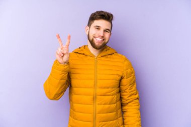 Mor arka planda izole edilmiş genç adam neşeli ve kaygısız parmakları olan bir barış sembolü gösteriyor..