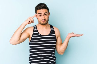 Kafkasyalı genç adam mavi arka planda izole edilmiş ve elinde bir ürün tutuyor..