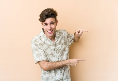 Beyazlı genç adam bej arka planda izole edilmiş. İşaret parmaklarıyla işaret ettiği için heyecanlı..