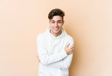 Beyaz tenli genç adam bej arka planda izole edilmiş gülüyor ve eğleniyor..