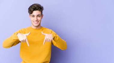 Mor arka planda izole genç beyaz adam parmaklarıyla aşağı noktalar, olumlu duygu.