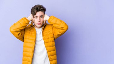 Kafkasyalı genç adam mor arka planda izole edilmiş kulakları kulaklarıyla kapatıyor çok fazla ses duymamaya çalışıyor..