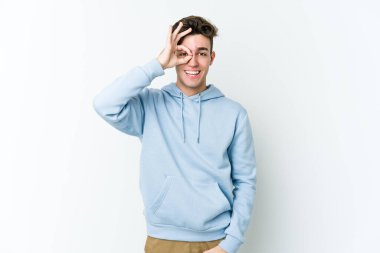 Beyaz arka planda izole genç beyaz adam heyecanlı tamam göz jesti tutmak.