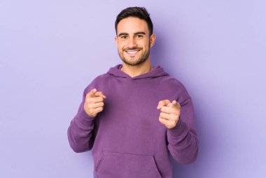 Mor arka planda izole edilmiş genç beyaz adam parmaklarıyla ön tarafı işaret ediyor..