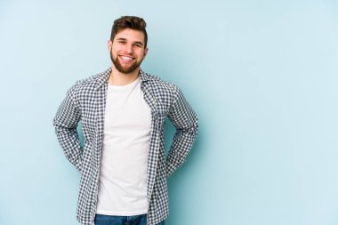 Mavi arka planda izole edilmiş genç beyaz adam mutlu, güler yüzlü ve neşeli.